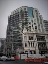 Load image into Gallery viewer, The International Apartments showing the scaffolding layers to allow for demolition and construction of the new building