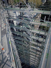 Load image into Gallery viewer, The International Apartments under construction with scaffolding layers to allow for demolition and construction of the new building