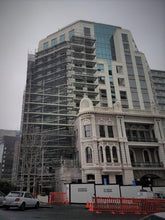 Load image into Gallery viewer, The International Apartments showing the scaffolding layers to allow for demolition and construction of the new building

